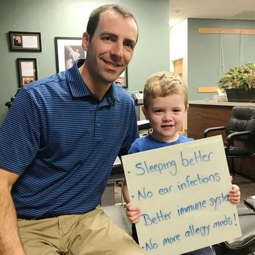 Jess’s son holding a sign that reads: Sleeping better, No ear infections, Better immune system, No more allergy meds!
